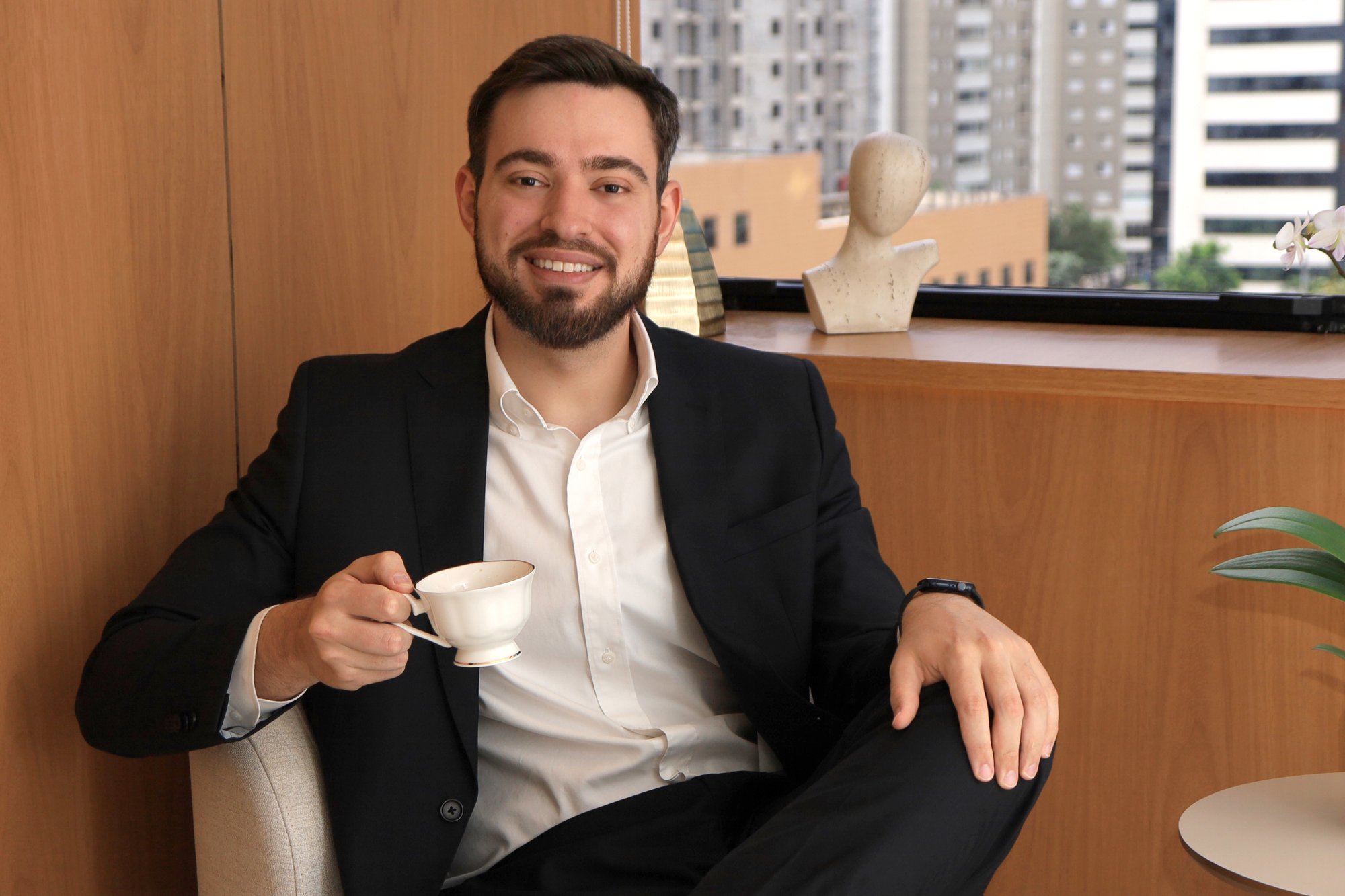 Dr. Henrique Dalmolin, reumatologista, com uma xícara de café na sala de espera do consultório em Moema