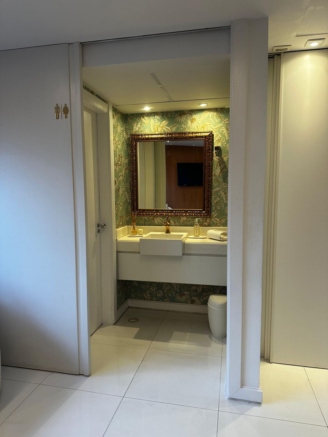 Lavabo do consultório com papel de parede botânico e espelho dourado