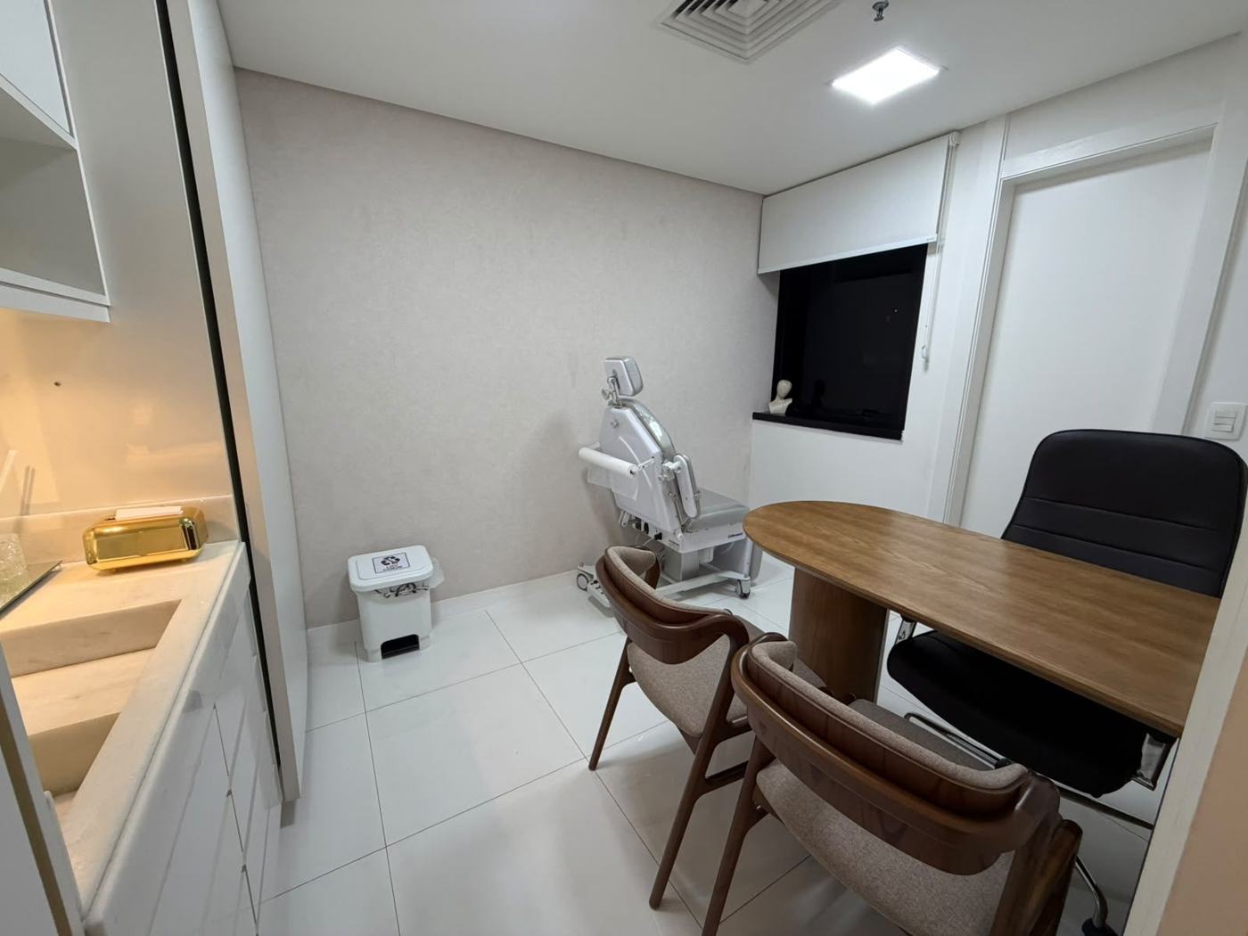Sala de atendimento com mesa de madeira e maca de exame